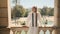 Young posh woman in stylish white suit standing on old balcony with beautiful view on park