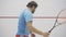 Young positive coach showing thumb up to sportsman playing squash in gym. Portrait of concentrated mid-adult bearded man