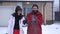 Young positive couple standing in the backyard in front of the large house under falling snow. Bearded man and