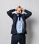 Young positive handsome man in official costume standing, biting tie, holding head with hands and feeling stressed