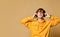 Young positive teen boy in yellow hoodie, sunglasses and headphones standing and smiling