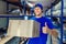 A young positive warehouse worker holds a cardboard box in his hands and smiles.