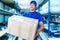 A young positive warehouse worker holds a cardboard box in his hands and smiles.