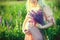 Young pregnant blonde woman in a pink dress holds her hands on her swollen belly with a bouquet of violet field flowers, among the