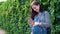 Young pregnant girl dressed in overalls looking at phone, on green background.