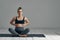 Young pregnant millennial woman sitting on the mat touches her belly after performing prenatal and meditation exercises