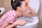 Young pregnant tired woman with pain is vomiting in toilet sitting on the floor at home.