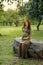 Young pregnant woman in anticipation of a baby sitting on a big stone in a park in the sun rays