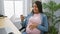 Young pregnant woman business worker watching video on smartphone touching belly at the office