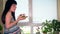 Young pregnant woman eating tasty cake sitting near window at home