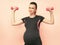 Young pregnant woman exercises with dumbell. Working out and fitness on last months of pregnancy and healthy motherhood concept.