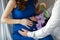 Young pregnant woman with future father in a blue dress holds her hands on her swollen belly, love concept, violet flower