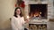 A young pregnant woman in glasses sits by the fireplace with a sparkler in her hand. Christmas mood.