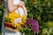 A young pregnant woman in her white dress embraces her stomach, with a basket of flowers in the middle of a sunflower field