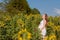 A young pregnant woman in her white dress embraces her stomach, with a basket of flowers in the middle of a sunflower field.