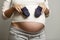 A young pregnant woman holds booties in her big belly. Happy expectation of birth and tenderness. Gray background. Close-up