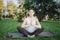 Young pregnant woman sit on yoga mate and pray outside in park. She keep hands close and sit in lotus pose. Model hold