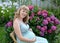 The young pregnant woman sits against the background of a bush of the blossoming hydrangea in a garden