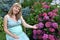 The young pregnant woman sits in a garden near a bush of the blossoming hydrangea