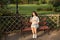 Young pregnant woman sitting on bench in park and holds sneakers for newborn