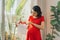 Young pregnant woman standing near big window with her future baby`s clothes