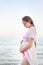 Young pregnant woman is standing on the seashore and hugging her belly. Enjoying the moment