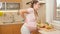 Young pregnant woman suffering from spinal pain holding hand on back and resting on kitchen after cooking and doing