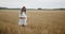 Young pregnant woman walking through a wheat field holding wheat bouquet