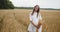 Young pregnant woman walking through a wheat field holding wheat bouquet