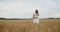 Young pregnant woman in white dress stands in a wheat field holding wheat