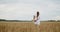 Young pregnant woman in white dress stands in a wheat field holding wheat