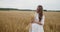 Young pregnant woman in white dress stands in a wheat field holding wheat