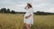 Young pregnant woman in white dress stands in a wheat field touching her belly