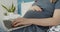 Young pregnant woman work on a laptop lying down on bed in domestic environment