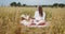 Young pregnant woman writing notes in a notebook during picnic in a wheat field