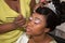 Young pretty american black woman getting her eyes make up done by professional artist using brush applying eyeshadow for wedding