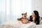 Young pretty Asian woman lying and placing hand on Shiba inu dog head on bed