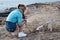 Young pretty blond woman, taking picture on her phone of her small husky puppy. Owner and the light grey dog, playing on the sandy