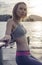 Young pretty blonde female wearing exercise clothing standing on the pier near the sea and enjoying early morning with beautiful