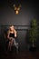 Young pretty blonde girl is sitting on the chair in evening shiny dress close up on the grey wall background in the photo studio