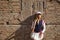 Young, pretty, blonde woman in white cap and skirt, jacket and baseball bat leaning against broken brick wall in background.