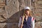 Young, pretty, blonde woman in white cap and skirt, jacket and baseball bat leaning against broken brick wall in background.