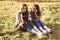 Young pretty brunette twin girls sitting on the grass with legs slightly bent in knees and looking in a brown book