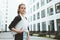 Young pretty business woman hold modern laptop looking away while standing in urban street