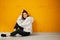 Young pretty calm relaxing girl in a white hoodie poses sitting on the floor against a yellow concrete wall.