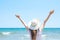 Young Pretty Caucasian Woman with Long Chestnut Hair in Hat Hands Lifted up in the Air Stands at Beach Looks at Turquoise Sea