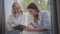 Young pretty Caucasian woman looking photos with older blond lady. Mother and daughter sharing memories at home. Happy