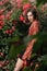 Young pretty female fashion model posing in front of rose bush. Cityscape portrait. Outdoor portrait of a romantic girl with hard