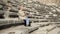 A young pretty female student is sitting on the steps of an ancient amphitheater