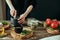 A young pretty girl grinds spices in a mortar while cooking a dish, fresh ingredients are spread out on a wooden table.